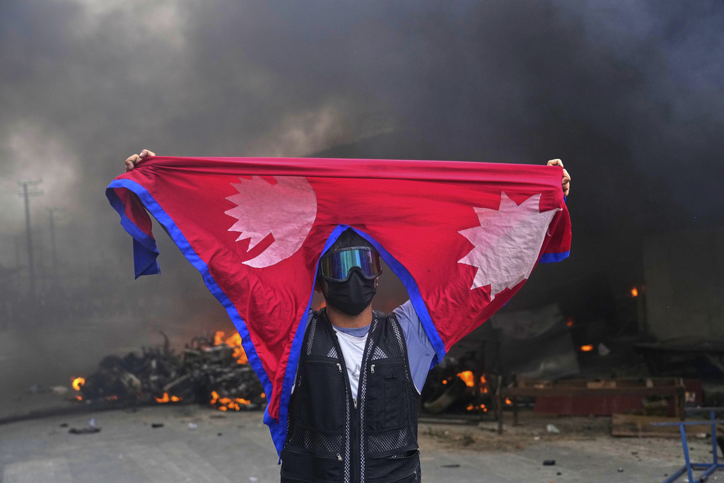 A protester shouts slogans carrying national flag after burning down a police station during protests against social media ban and corruption in Kathmandu, Nepal, Tuesday, Sept. 9, 2025. (Photo by Niranjan Shrestha / AP)